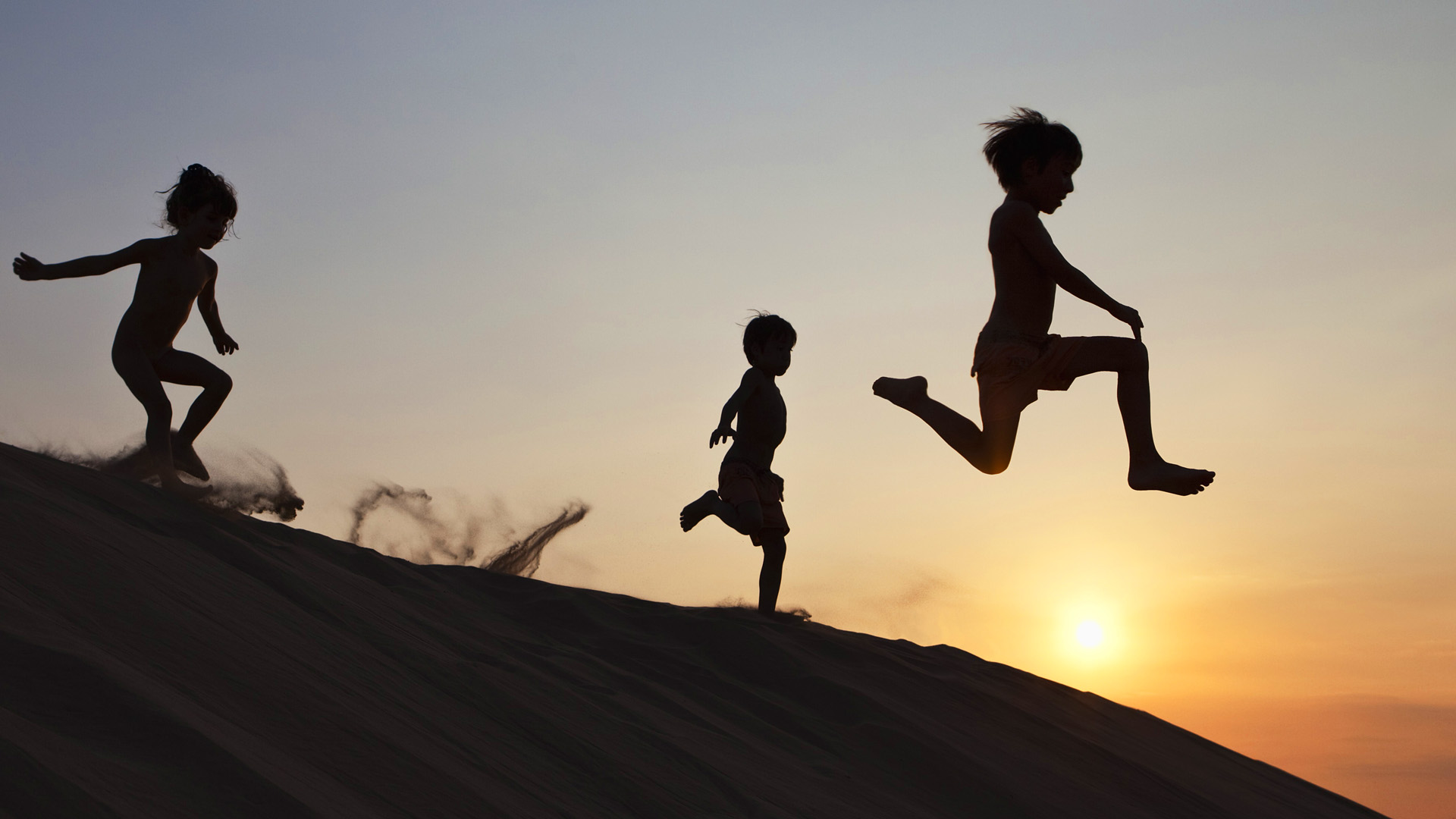 Children running down a sand dune