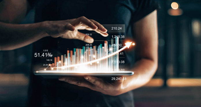 Businessman holding tablet and showing a growing virtual hologram of statistics, graph and chart with arrow up on dark background. Stock market. Business growth, planing and strategy concept.