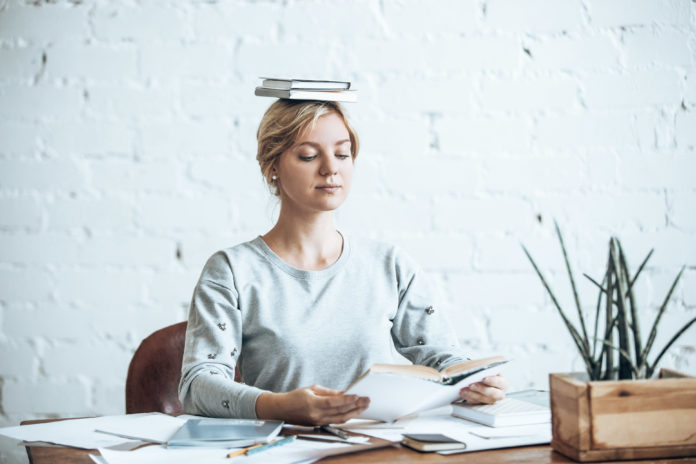 Portrait of woman at desk, books on her head